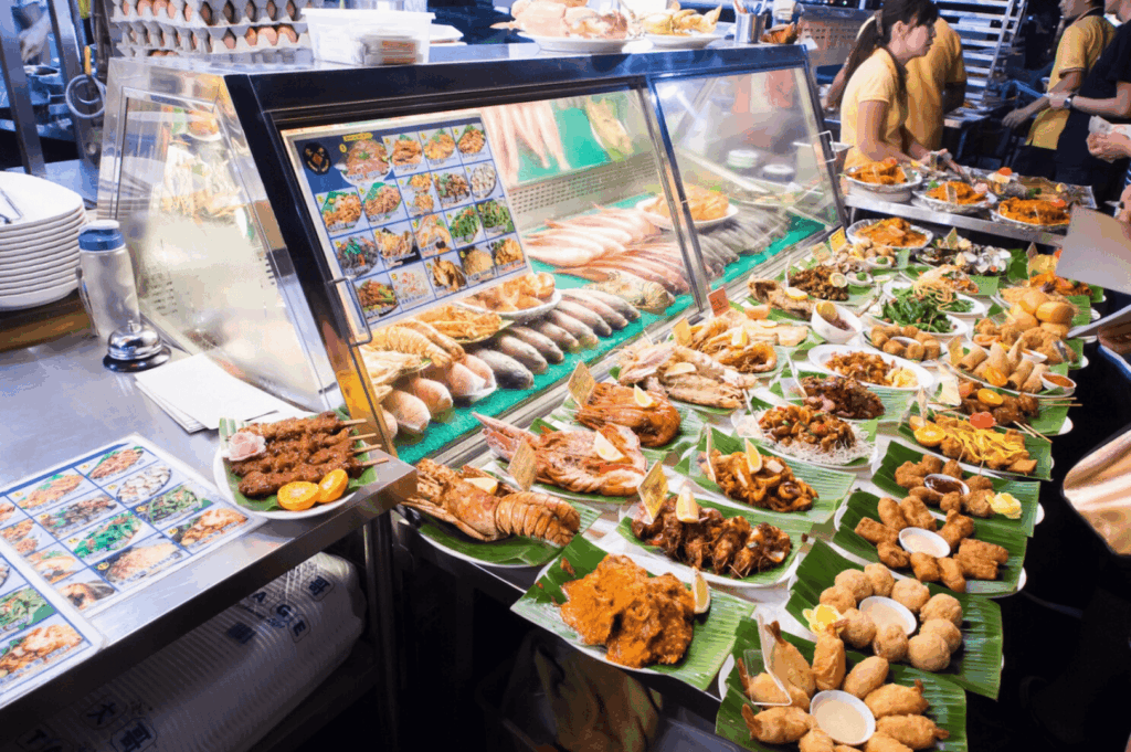 Colorful hawker food stall in a bustling hawker centre in Singapore, displaying delicious food like satay, noodles, grilled meats, seafood, sushi, and local dishes on banana leaves—representing the vibrant hawker culture and culinary diversity of singapore's hawker centres. Popular food stalls and hawker stalls at Maxwell Food Centre, Lau Pa Sat, Tiong Bahru Market, Satay Street, Airport Road Food Centre, and Little India serve hainanese chicken rice, char kway teow, nasi lemak, chilli crab, hokkien mee, and indian food. Located in the central business district near Marina Bay, City Hall, Orchard Road, and Tanjong Pagar, these open air food courts are a central location for expat life, lunch rush, and making new friends. A short walk from mass rapid transit, the subway system, and international schools, hawker centers are a must visit spot for expats moving abroad. With most stalls recently renovated and other stalls offering hidden gems praised by Anthony Bourdain, singapore's hawker centers reflect singapore's identity and have a significant impact on expat packages, school fees, health insurance, employment pass, property cost, and services. This hawker center guide offers advice, tips, and insights into food, business, living, and life in Singapore and Southeast Asia—a world-class destination to eat, connect with your home country, and explore the potential downsides and rewards of expat living.