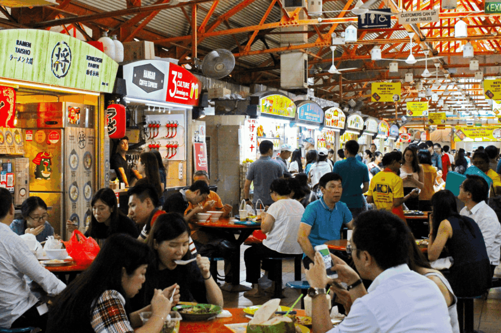 Crowded hawker centre in Singapore’s central business district during the lunch rush, with food stalls and hawker stalls offering delicious food in the country without potential downsides like hainanese chicken rice, char kway teow, nasi lemak, chilli crab, satay, hokkien mee, noodles, and other local dishes. This vibrant food centre reflects singapore's hawker centres and hawker culture, featuring street food vendors and open air food courts near Marina Bay, City Hall, Orchard Road, and Tanjong Pagar. Popular destinations like Maxwell Food Centre, Lau Pa Sat, Tiong Bahru Market, Satay Street, Airport Road Food Centre, and Little India showcase singapore's identity and hidden gems praised by Anthony Bourdain. Located near mass rapid transit, the subway system, and international schools, hawker centers are a central location for expat life, moving abroad, and making new friends. With most stalls recently renovated and other stalls serving indian food and Chinatown specialties, hawker centers have a significant impact on expat packages, school fees, health insurance, employment pass, property cost, and services. This hawker center guide offers advice, tips, and insights into food, business, living, and life in Southeast Asia—a must visit spot to eat, connect with your home country, and experience the world of local food culture.