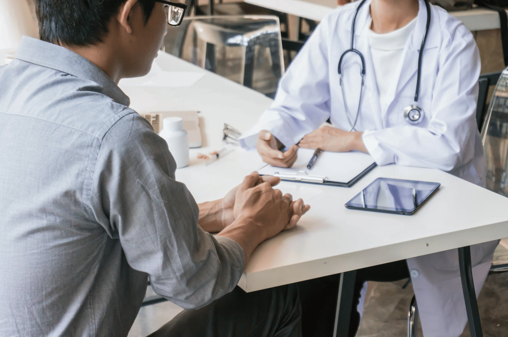 Healthcare professional in white lab coat consults with a seated patient across a clinic table, discussing treatment options with medication, tablet, and paperwork visible—capturing the personalized care and clinical transparency central to Singapore’s medical system.