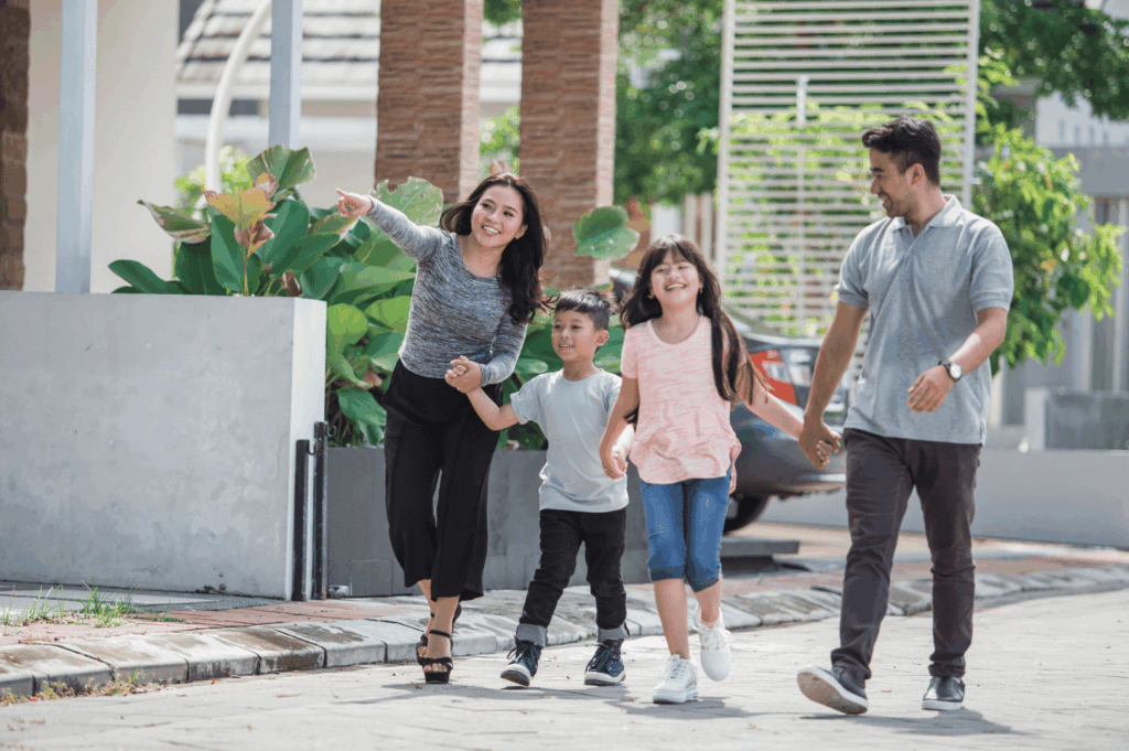 Smiling family of four walks hand-in-hand through a leafy residential neighborhood—reflecting the everyday health, safety, and quality of life supported by Singapore’s holistic healthcare system.