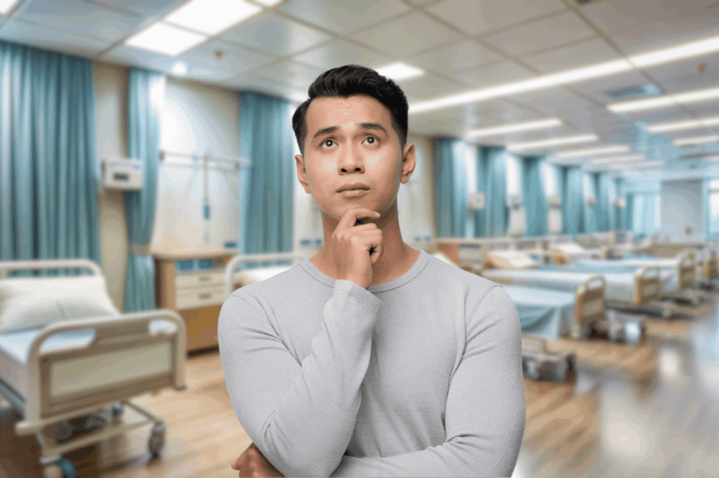 Thoughtful individual stands in a clean, well-lit hospital ward with neatly arranged beds and blue privacy curtains—evoking Singapore’s modern, orderly approach to shared patient care and clinical infrastructure.