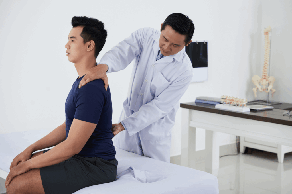 Healthcare professional in white lab coat performs a hands-on spinal assessment on a seated patient in a clinical setting—showcasing Singapore’s emphasis on musculoskeletal care, diagnostic precision, and patient-centered treatment.