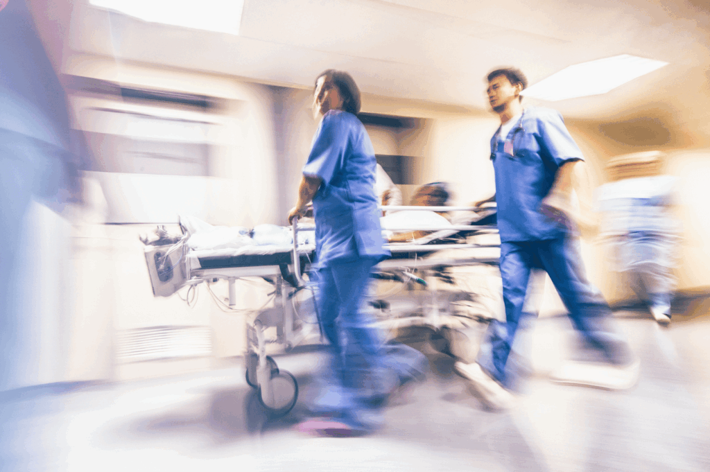 Medical personnel in blue scrubs rush a patient on a stretcher through a hospital hallway—capturing the swift, coordinated emergency response that defines Singapore’s high-functioning healthcare system.