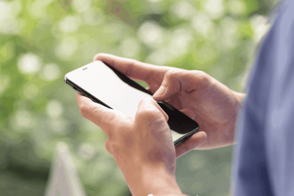 Close-up of hands interacting with a smartphone against a backdrop of green foliage—symbolizing Singapore’s embrace of mobile health technology and digital access to healthcare services.