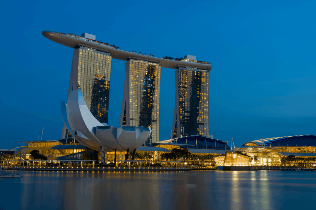 Evening view of Marina Bay Sands in Singapore, with illuminated towers and the ArtScience Museum in the foreground—an iconic destination easily accessible via Singapore’s MRT system. This Singapore MRT Guide for Expats highlights MRT rides across MRT lines including the North South Line, East West Line, Circle Line, Downtown Line, North East Line, Thomson East Coast Line, and LRT lines such as Bukit Panjang LRT. Expats can explore Singapore with cost-effective public transport options like bus rides, public buses, and train services, using contactless bank cards, mobile wallets like Apple Pay, Samsung Pay, Fitbit Pay, or physical cards such as EZ-Link, NETS FlashPay, and travel cards from other countries. MRT stations and train stations including Dhoby Ghaut, City Hall, Chinatown MRT, Marina Bay, Orchard Road, Raffles Place, Botanic Gardens, and Tanjong Pagar are accessible during peak hours, off peak hours, rush hours, off peak times, and midnight daily. The MRT map supports journey planning with Google Maps, SimplyGo app, MyTransport app, and the official app. Riders can pay directly and simply tap at ticketing machines or convenience stores using single trip tickets or the Singapore Tourist Pass. Features include train frequency, operating hours, priority seats, admin fee info, first bus timings, interchange stations, and total distance coverage across one line or multiple transfers on Singapore’s mass rapid transit network.
