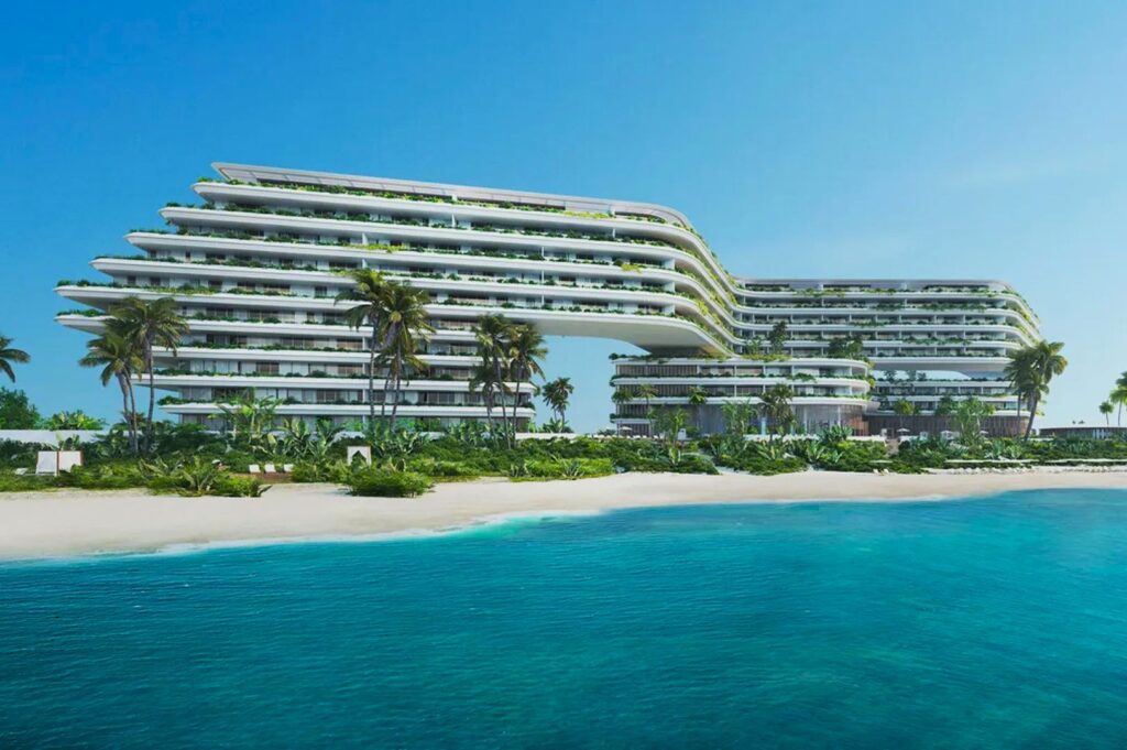 Futuristic beachfront hotel with curved architecture, surrounded by palm trees. The building overlooks a turquoise ocean under a clear blue sky.