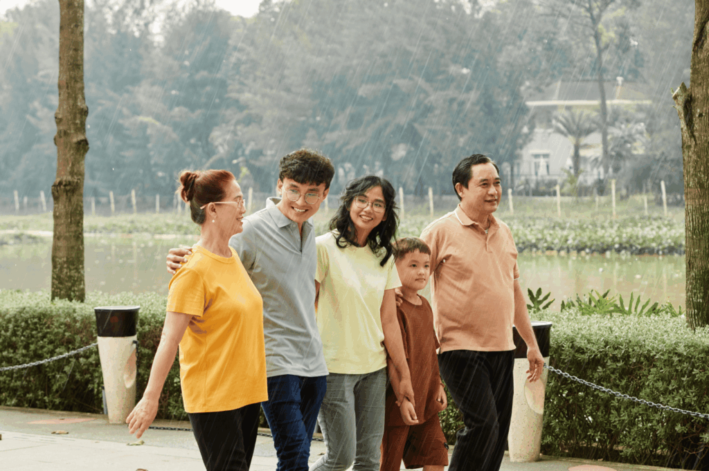 Five people walk together near a lakeside path on a rainy day, dressed in casual, weather-ready outfits. Their smiles and relaxed interactions reflect the joy of shared outdoor moments, even in Singapore’s unpredictable climate. Lightweight layers, rain-friendly fabrics, and a spirit of adaptability highlight the essentials of a practical expat wardrobe built for connection and spontaneity.