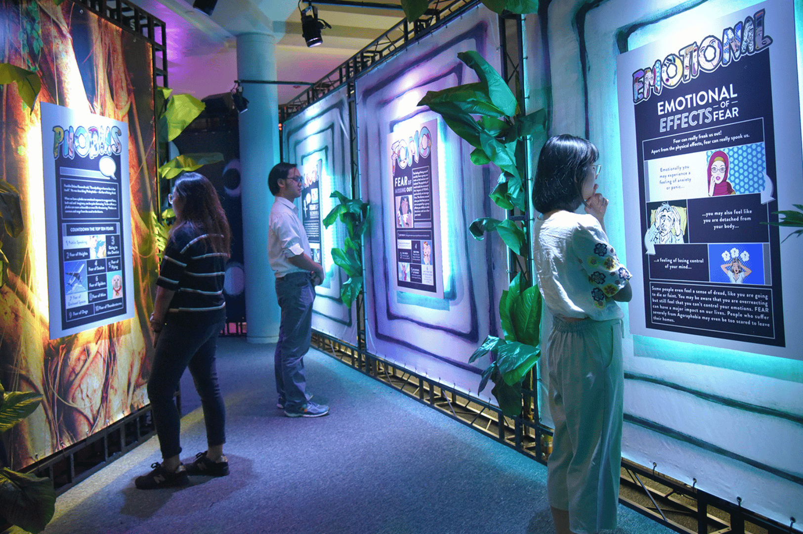 Families explore a colorful interactive exhibit in a Singapore science museum, where panels on phobias, fear, and emotions use vibrant graphics and playful design to make psychology engaging for children. The immersive setup with abstract art and greenery creates a fun, educational environment that sparks curiosity about how feelings shape human behavior.