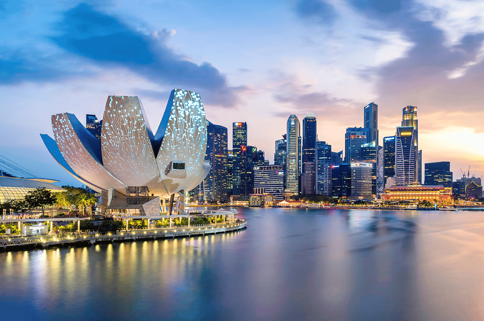 Twilight view of Singapore’s Marina Bay with the lotus-shaped ArtScience Museum glowing against the skyline. The illuminated museum, surrounded by skyscrapers reflecting in the bay, highlights one of the city’s most iconic family attractions where art, science, and interactive exhibits inspire curiosity for kids and adults alike.