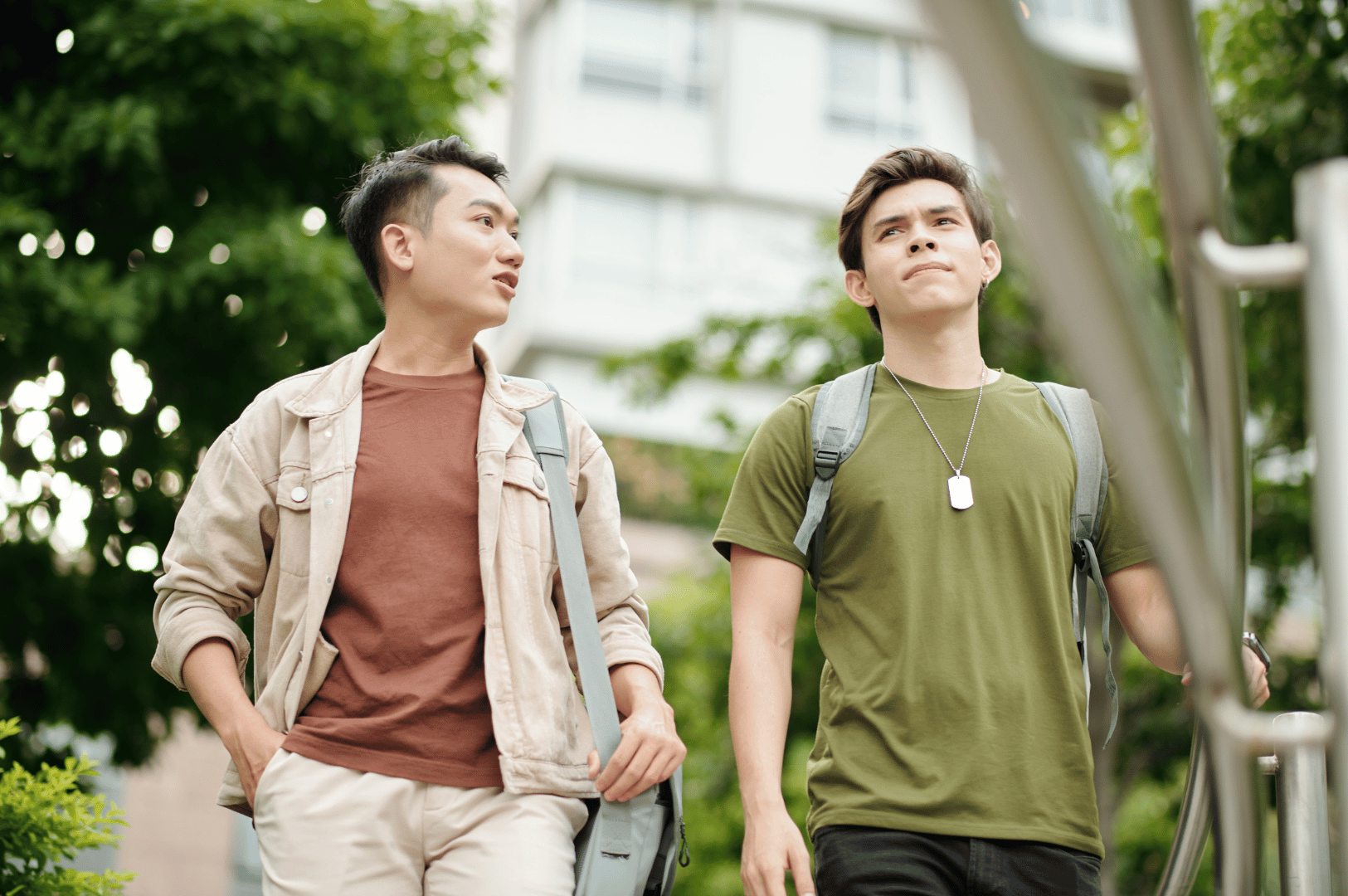 Two casually dressed young men walking and chatting in a leafy urban setting, each carrying a backpack; a relaxed, everyday moment that reflects how Singlish phrases like “can meh?” and “steady lah” naturally flow through campus life and street conversations in Singapore.