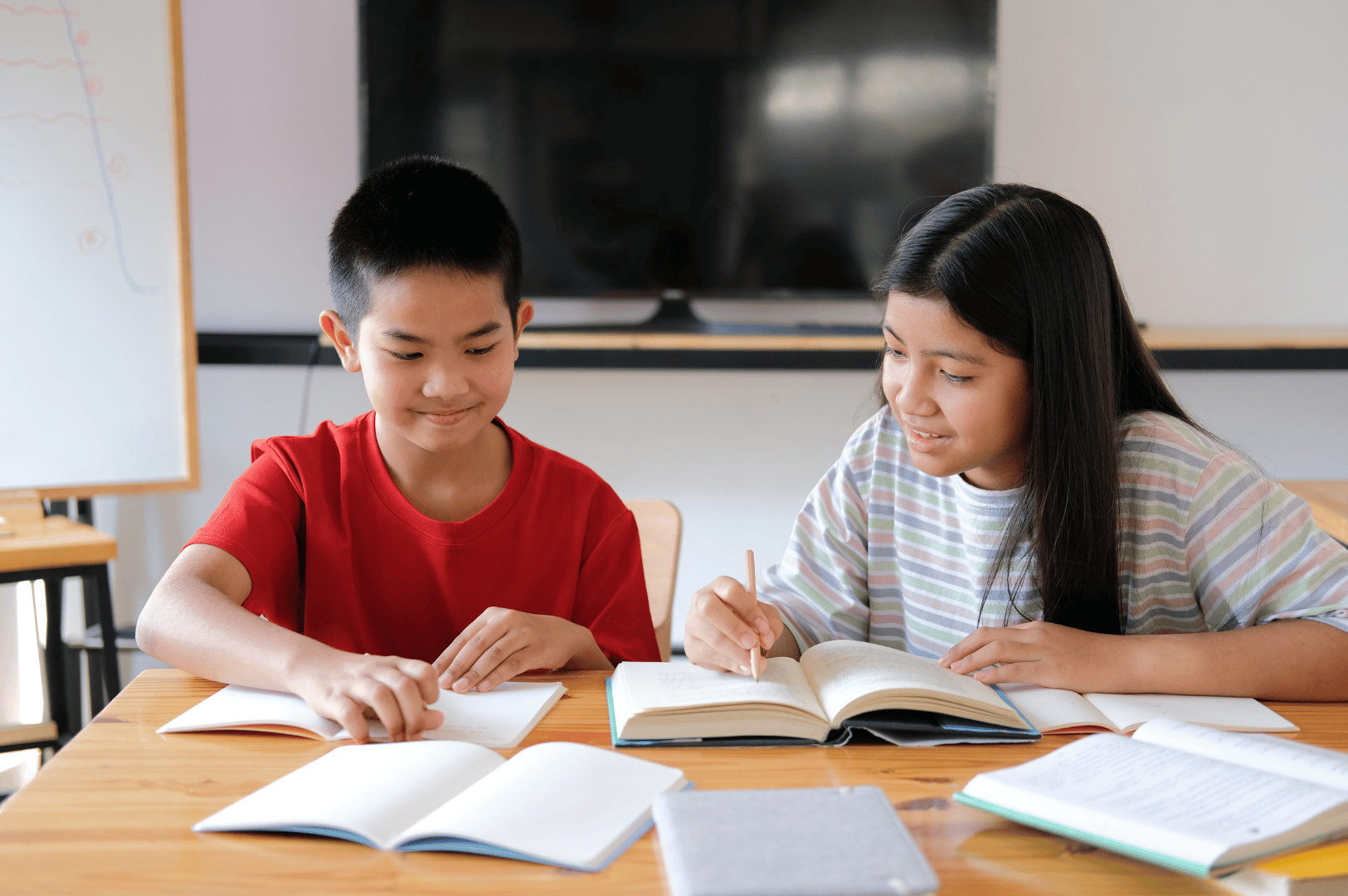 Two children sit at a wooden table, immersed in homework with open books and scattered papers—capturing the everyday rhythm of Singapore’s tuition culture, where peer learning and home-based study environments reinforce academic discipline and shared effort.