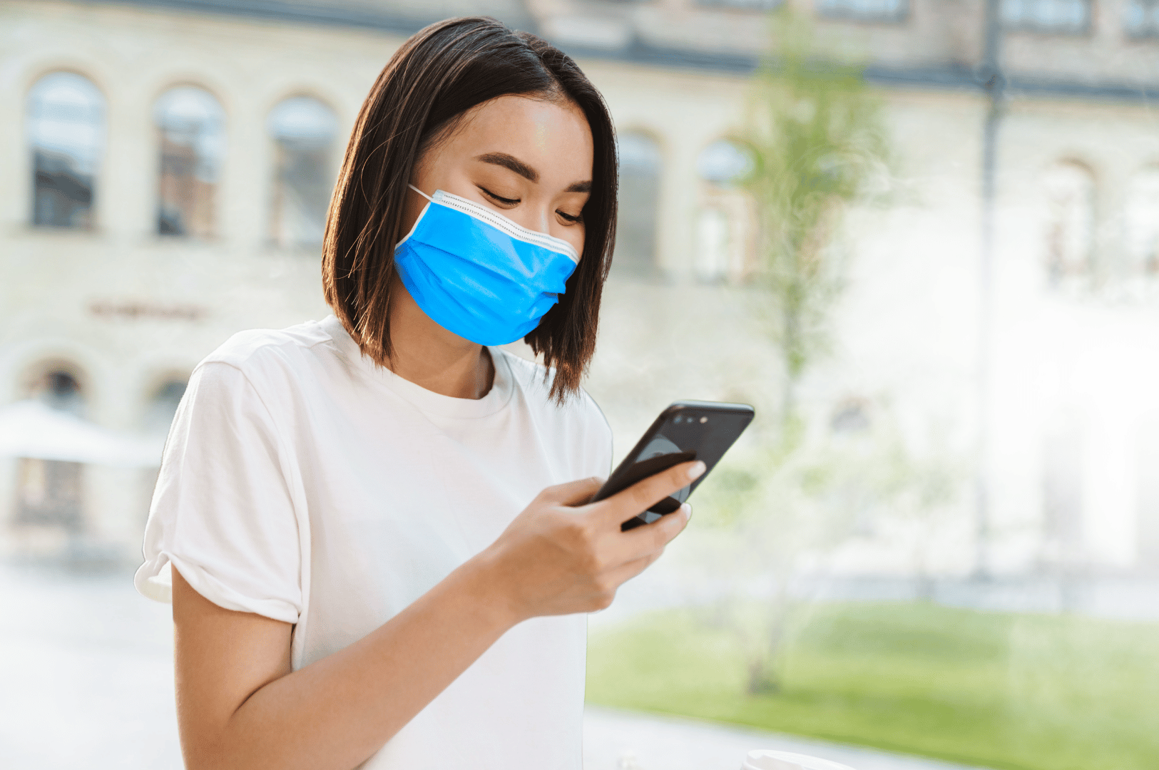 Person wearing a blue face mask outdoors, checking health updates on a phone during haze season