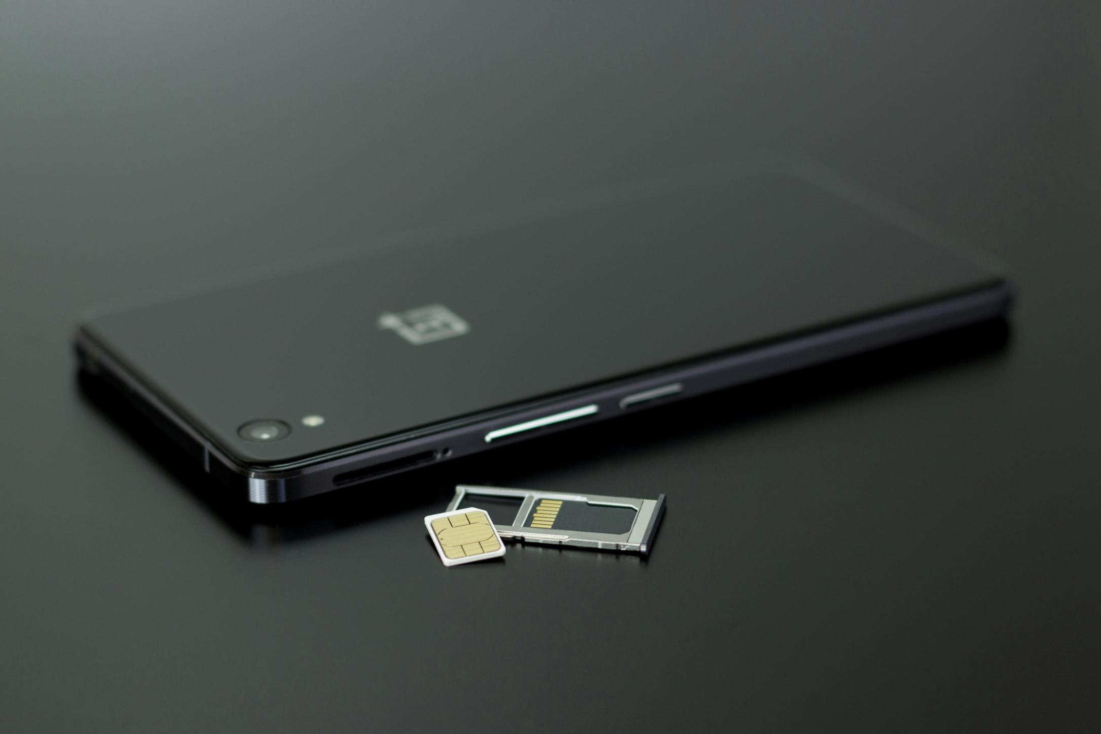 An image of a black mobile phone with its sim tray out as it sits on a black tabletop.
