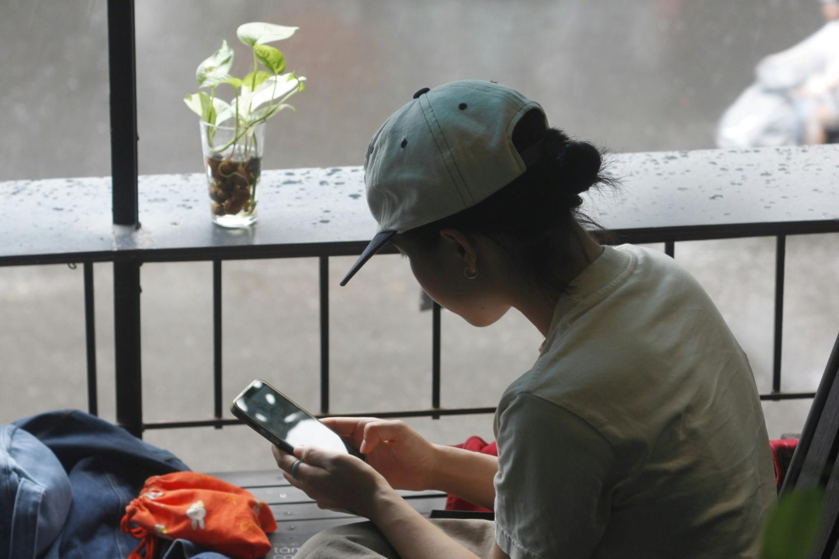 An image of a young woman using her phone inside a cafe on a gloomy day.