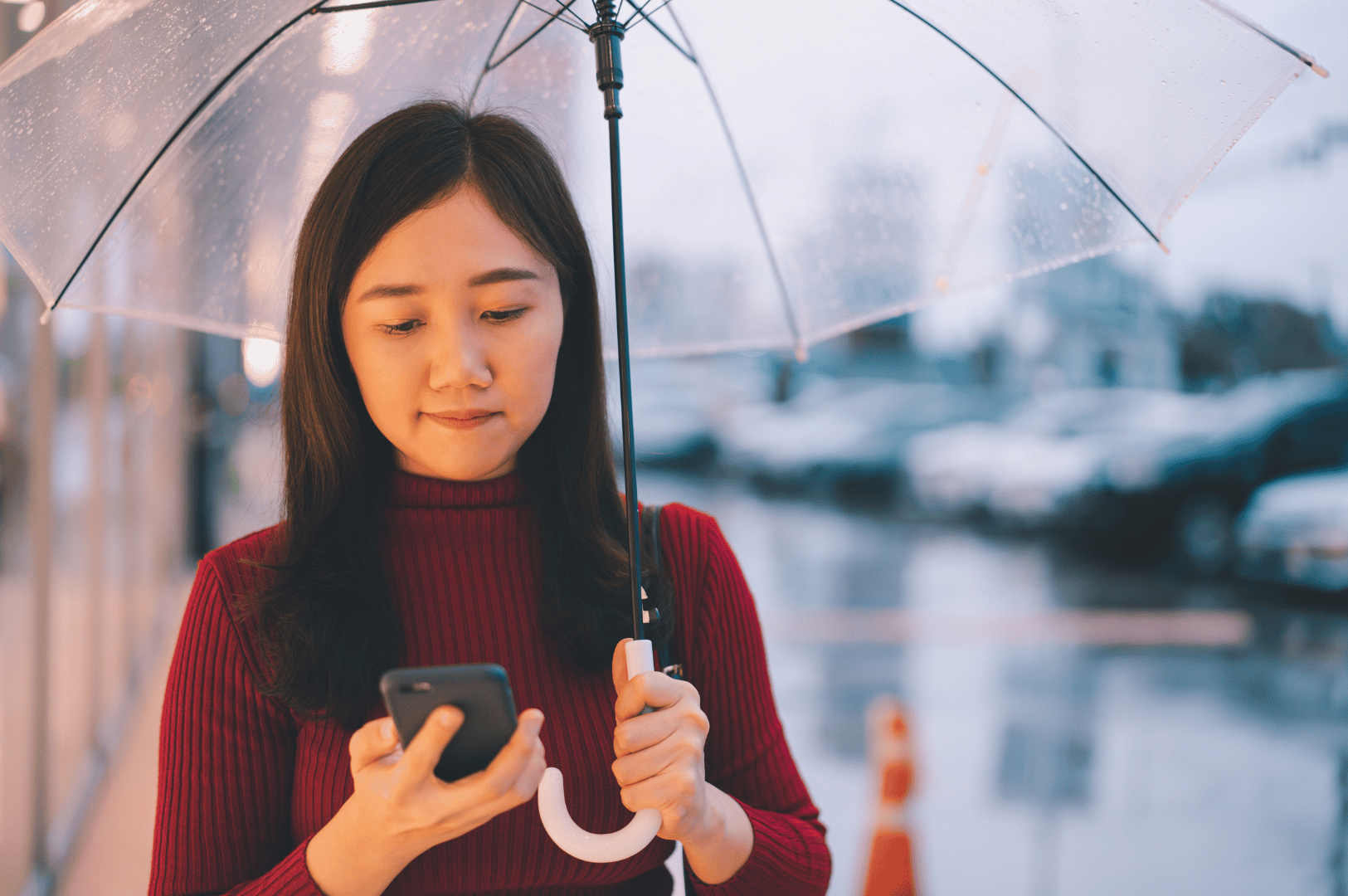 Woman holding a clear umbrella and checking her phone on a wet city street during heavy rain in Singapore.