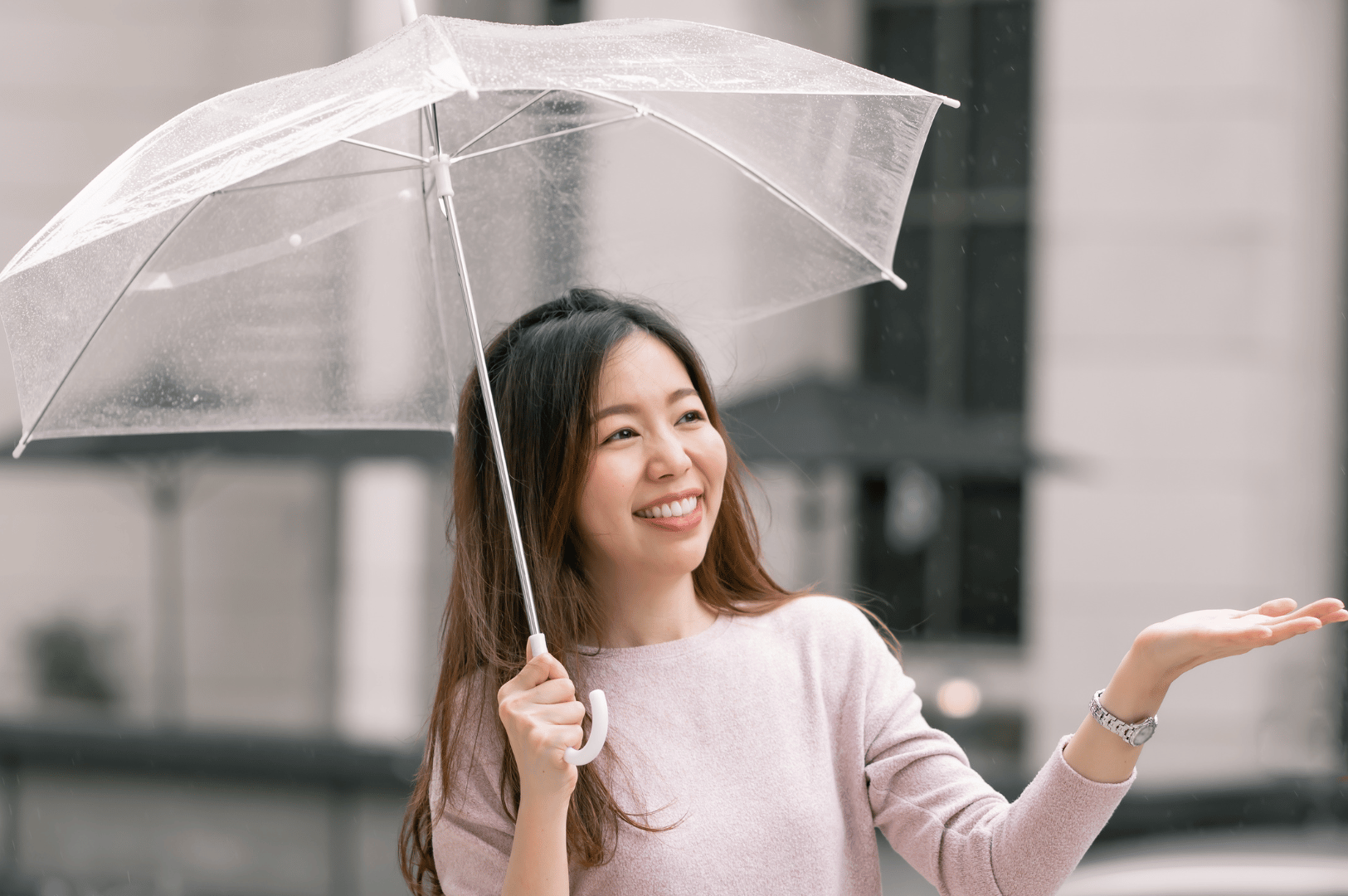 Smiling person under a clear umbrella during light rain in an urban Singapore setting, illustrating preparedness for monsoon showers.