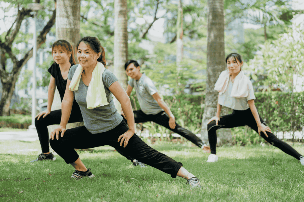 Four people stretching together on a grassy field in a Singapore park, promoting group fitness and active lifestyles in the city’s green outdoor spaces.