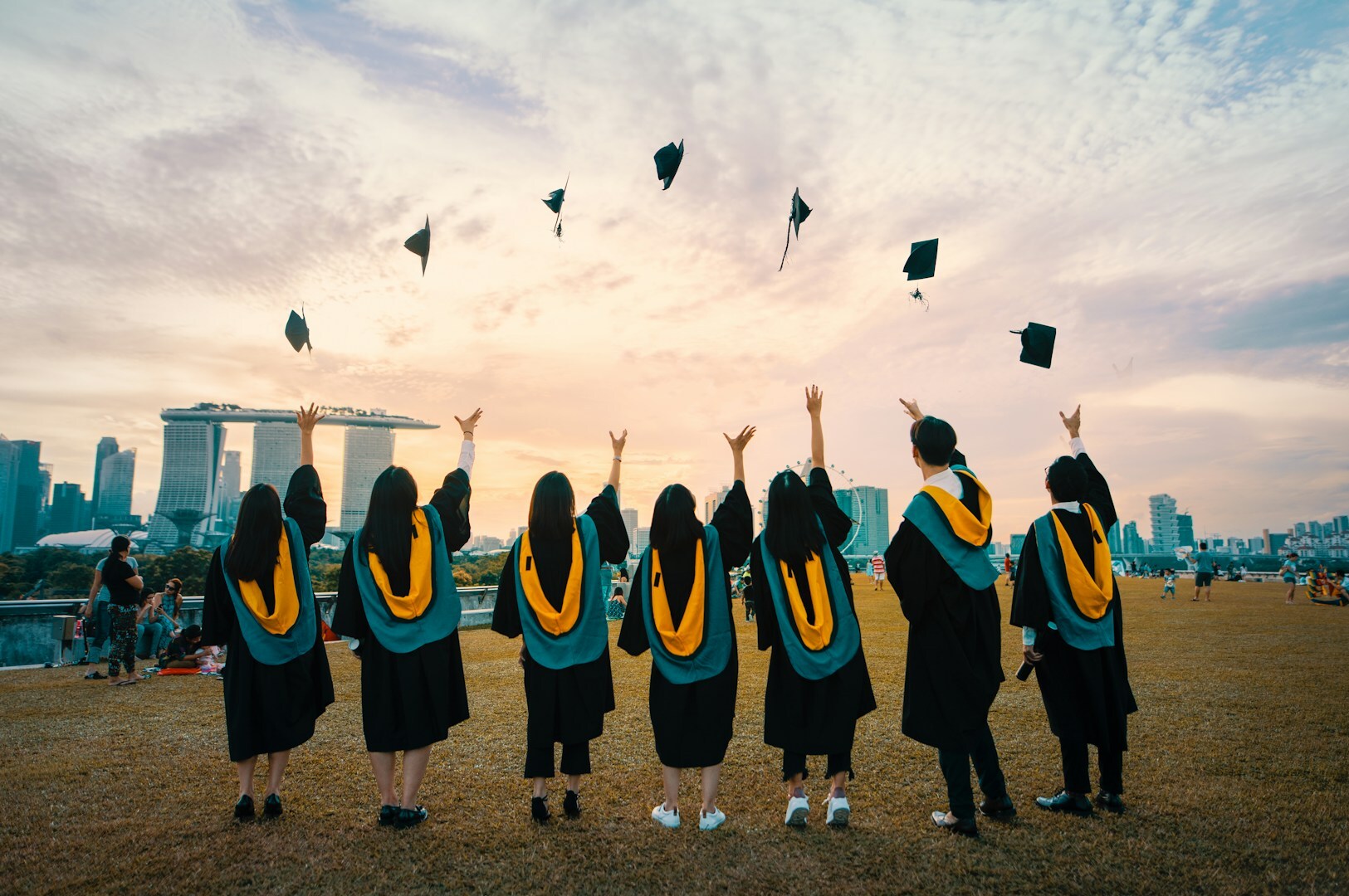 A group of Singaporean graduates celebrates by throwing their caps into the air, marking their academic achievement.