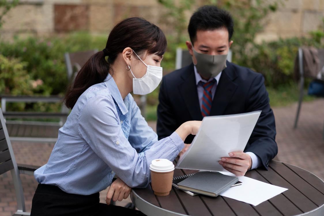 A photo of two employees going over their work as they sit outside a cafe for a coffee.
