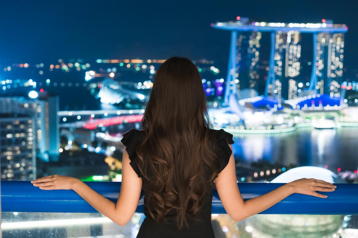 A picture of an individual looking over the bright city skyline of the night hours of Singapore.