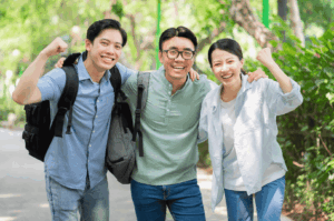 Three young adults stand on a sunlit path surrounded by lush greenery, dressed in lightweight, casual outfits ideal for Singapore’s tropical climate. Their relaxed smiles and raised arms suggest comfort and confidence, with breathable fabrics, short sleeves, and practical accessories like backpacks reflecting a functional yet stylish expat wardrobe.
