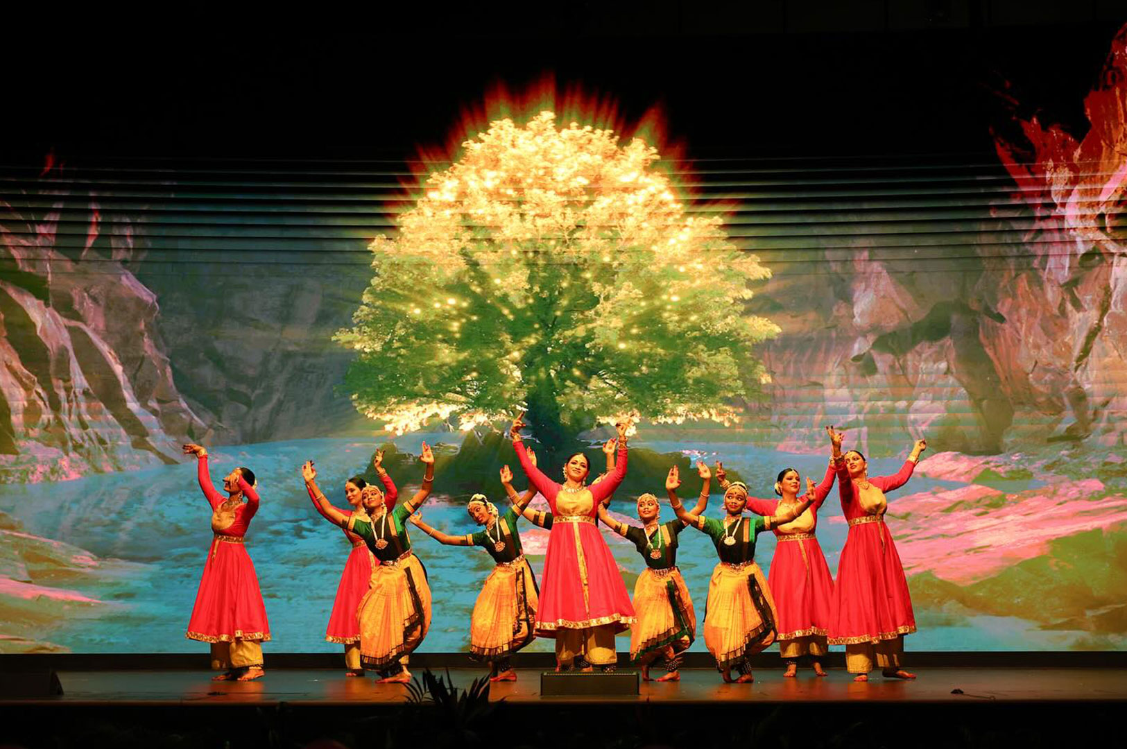 Group of dancers performing on stage with a glowing tree backdrop.