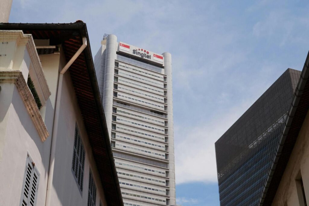 A low angle photo of the Singtel tower in Singapore surrounded by other infrastructures.