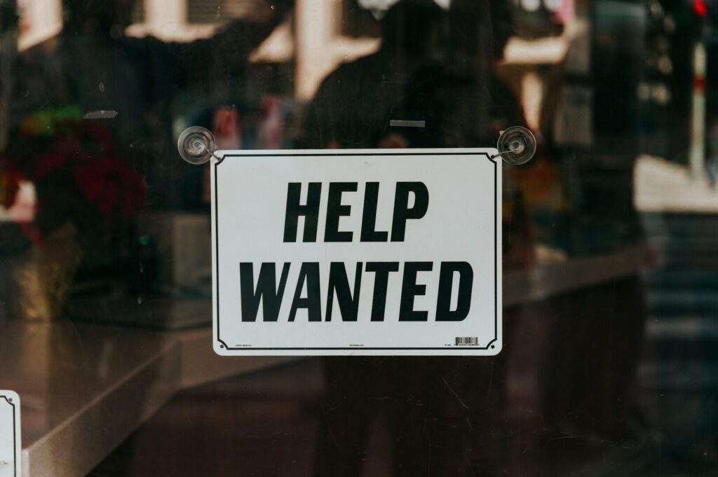 A "Help Wanted" sign prominently placed in a storefront window, signaling employment opportunities at the business.