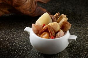 A bowl containing Buddha Jump Over the Wall, showcasing an assortment of ingredients, set against a black background.
