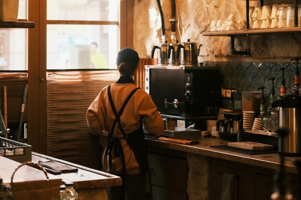 A person working at a coffee shop, serving customers and preparing beverages in a cozy environment.