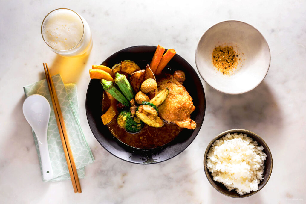Overhead view of Japanese Hokkaido soup curry set with rice, vegetables, and iced drink