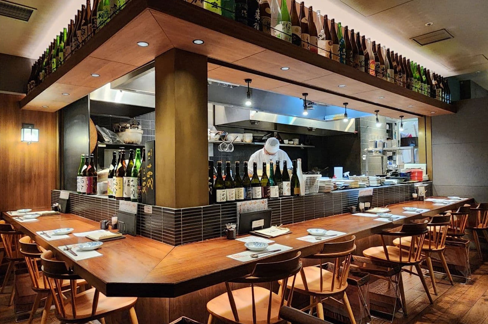 Cozy neighbourhood izakaya interior with wooden counter seating and open kitchen.