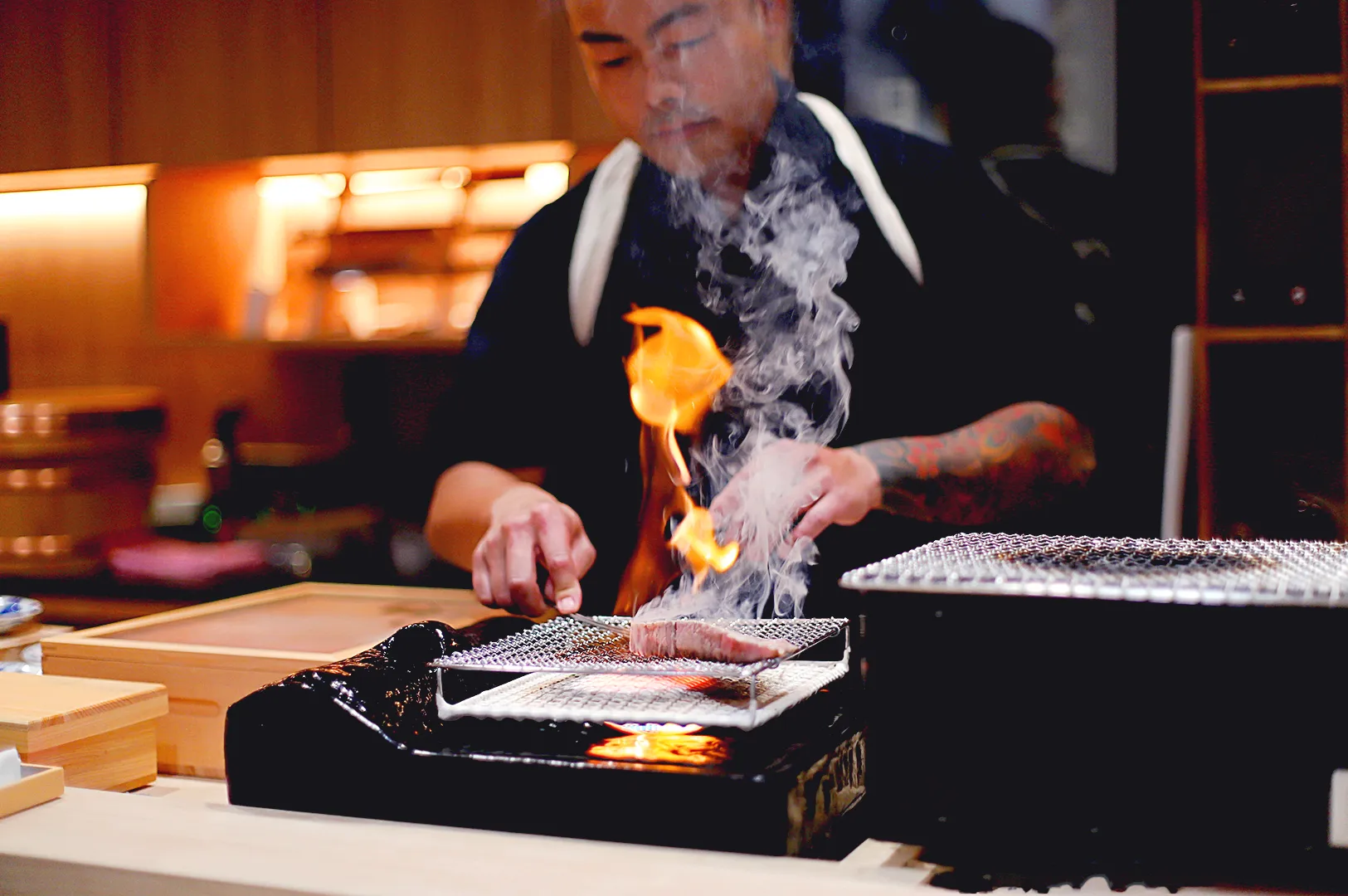 Chef torching premium sushi over flame at omakase restaurant