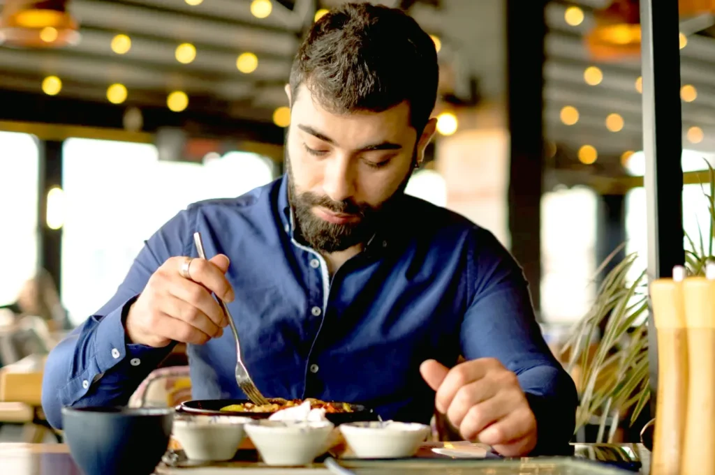 Man quietly eating a meal in a warm-lit restaurant, focusing on the textures and flavors of his food.