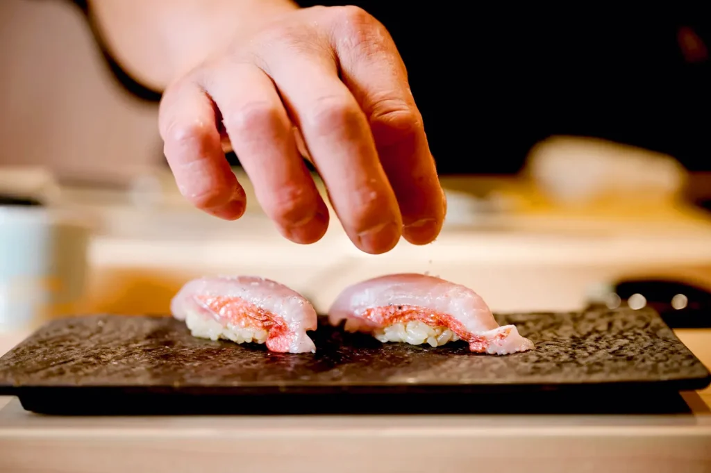 Chef hand placing fresh nigiri sushi on stone serving plate