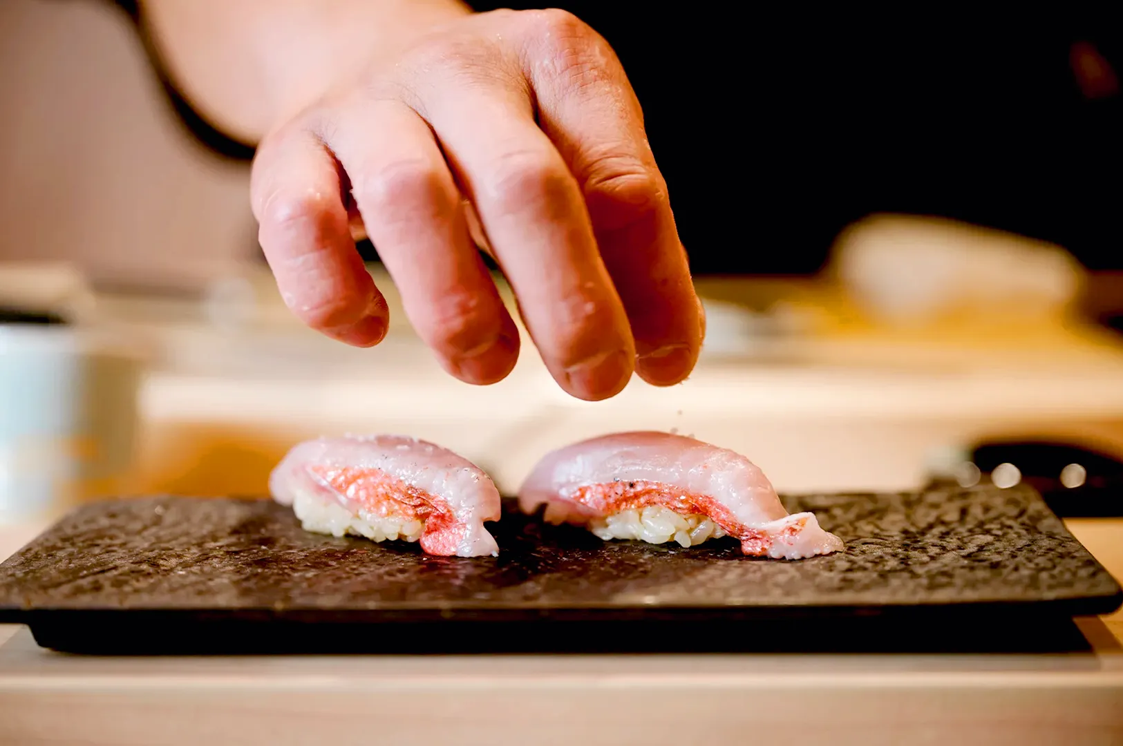 Chef hand placing fresh nigiri sushi on stone serving plate