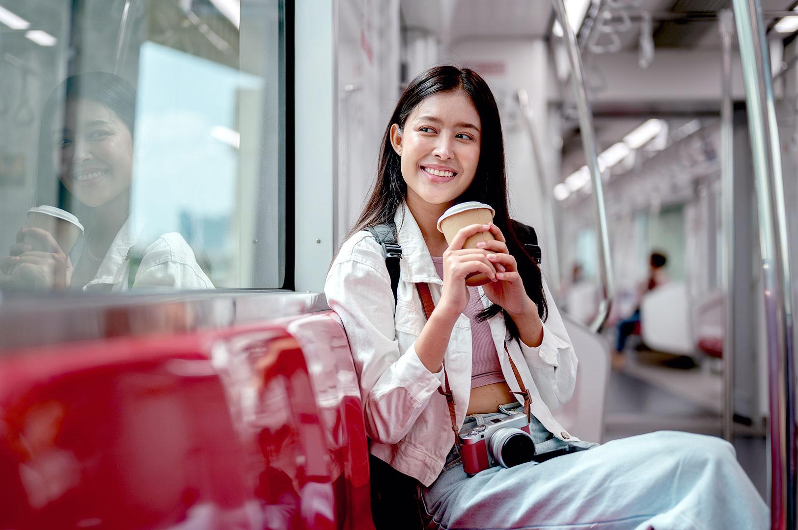 Expat woman commuting on Singapore MRT holding coffee and camera