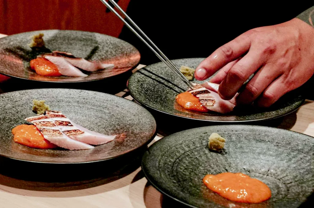 Fine dining sushi plating with seared fish and uni on ceramic dishes