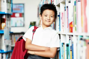 Primary school student in Singapore school uniform standing in library with books, representing student learning and expat education experience