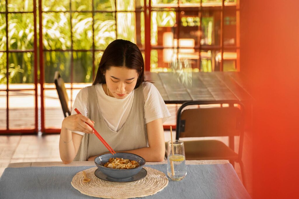 Woman eating alone at a shared table in a peaceful restaurant reflecting quiet connection and everyday dining culture