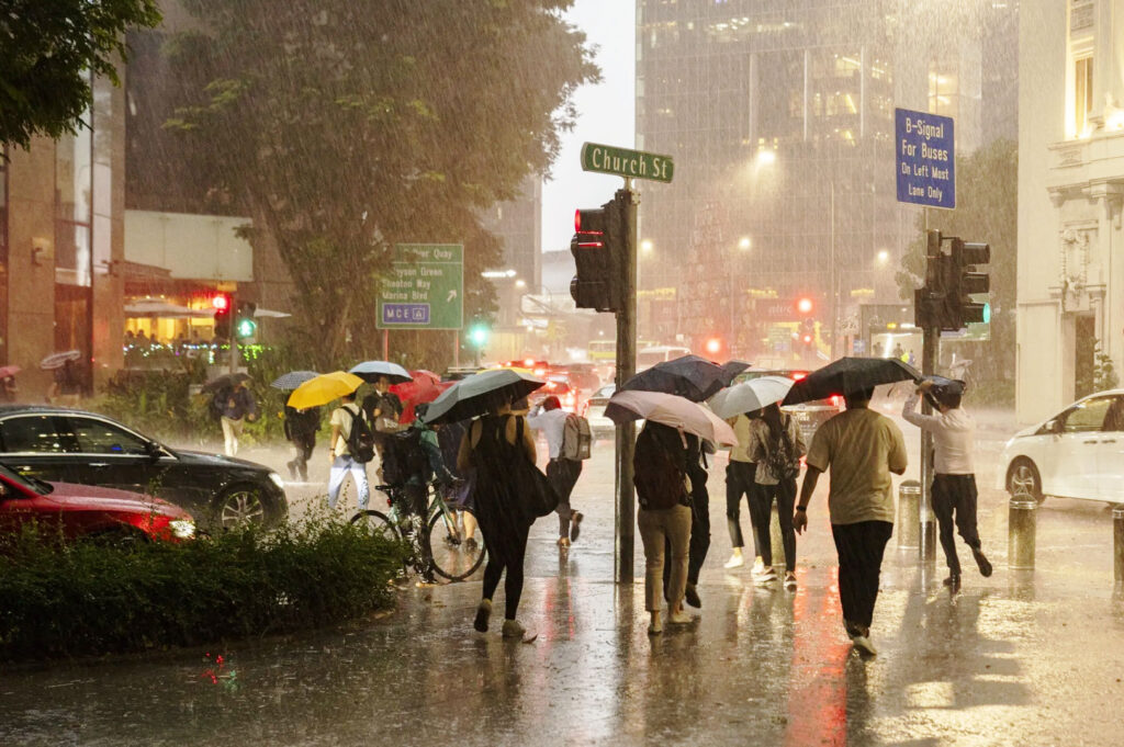 People walking through heavy rain in Singapore CBD with umbrellas during Northeast Monsoon season