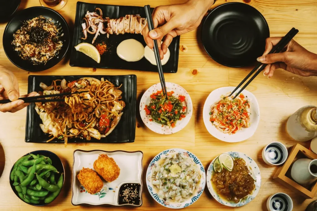 Overhead view of Japanese izakaya dining table with yakisoba, edamame, sake, and shared appetizers