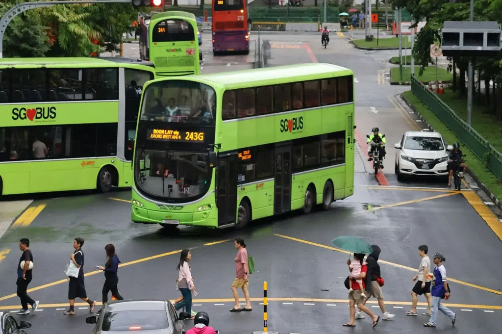 A vibrant green double-decker bus with an open-top upper deck traveling down a modern city street lined with lush tropical trees.