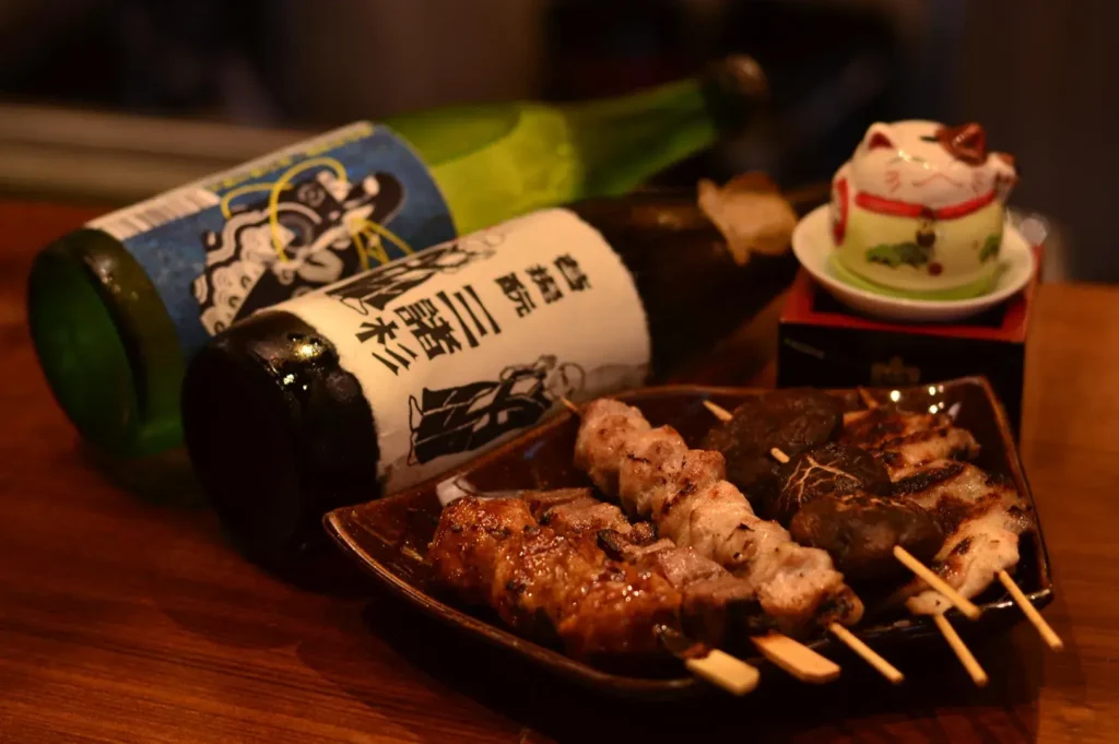 Japanese sake bottles paired with yakitori skewers and grilled mushrooms in cozy izakaya setting
