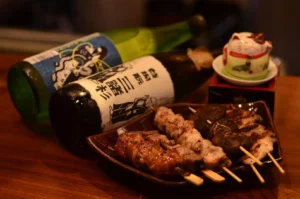 Japanese sake bottles paired with yakitori skewers and grilled mushrooms in cozy izakaya setting