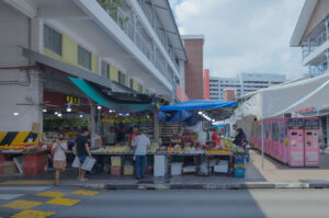 Outdoor fruit market stall in Singapore with colorful awnings, shoppers, and crates of fresh produce.