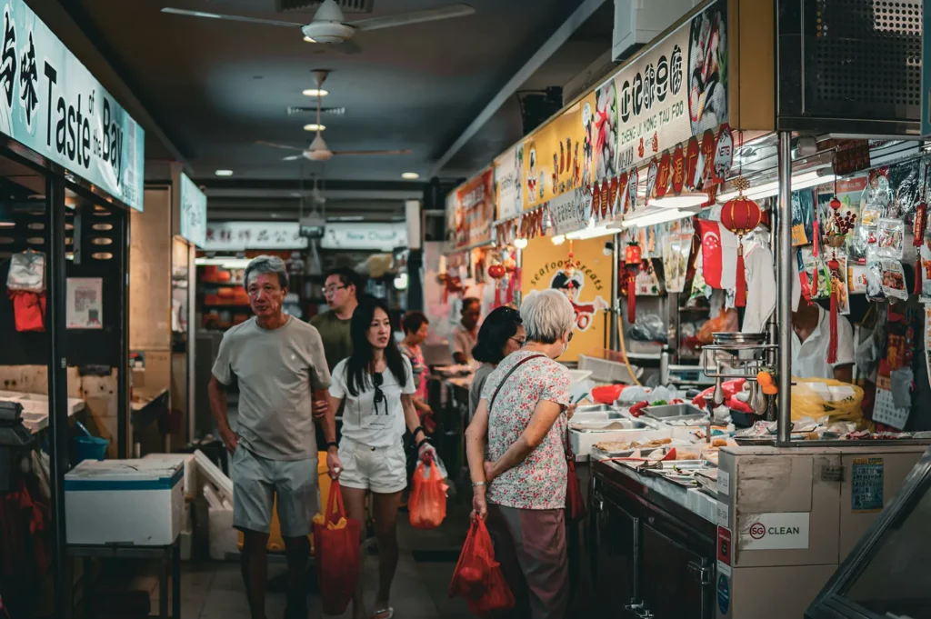 Shoppers walking through hawker center aisle with food stalls.