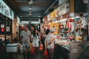 Shoppers walking through hawker center aisle with food stalls.
