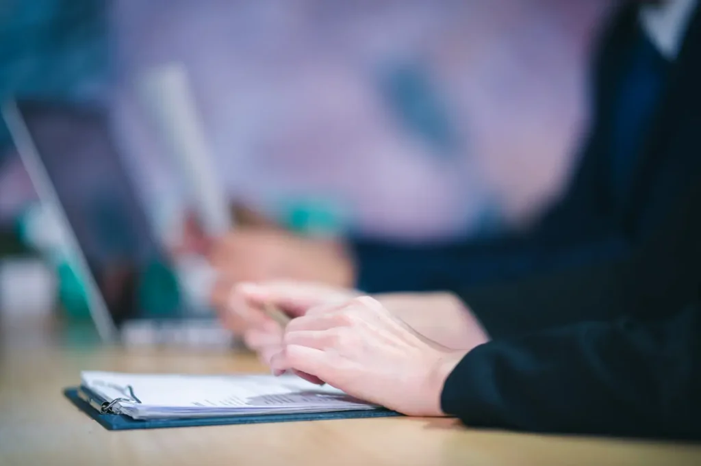 Close-up of hands on a clipboard and a laptop during a meeting.