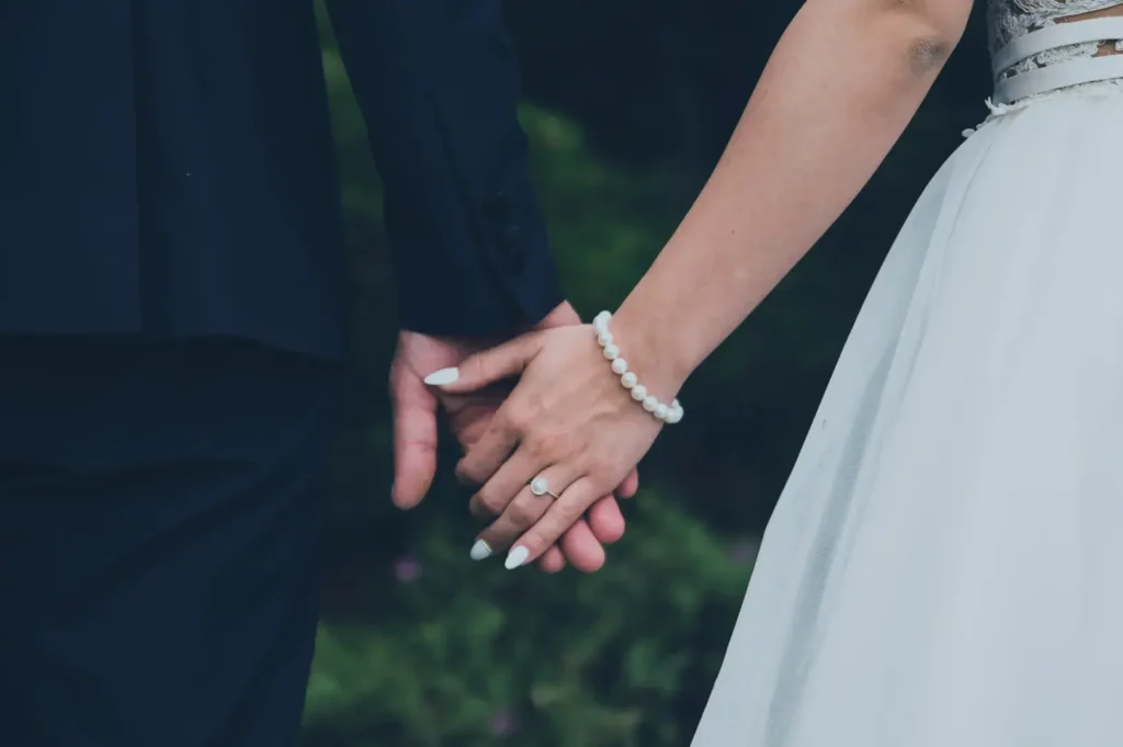 A close-up shot of a person in a black suit holding hands with a person in a white wedding dress.